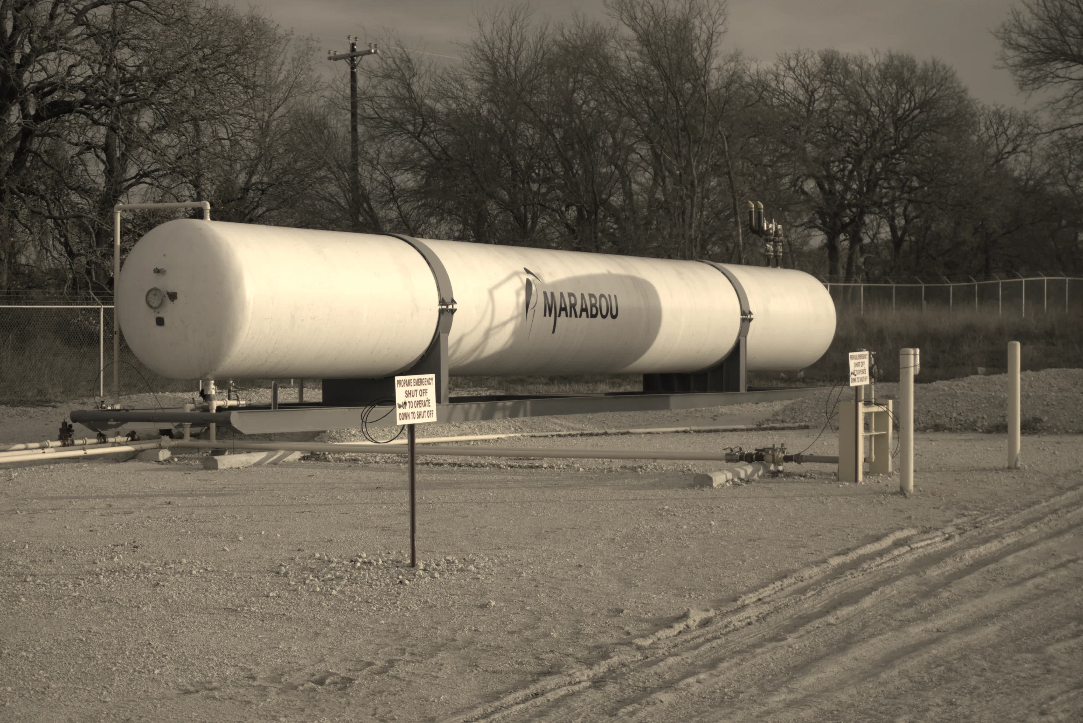 A horizontal bullet storage vessel on steel saddles at a fenced site, with connecting pipework and bollards on a graded pad