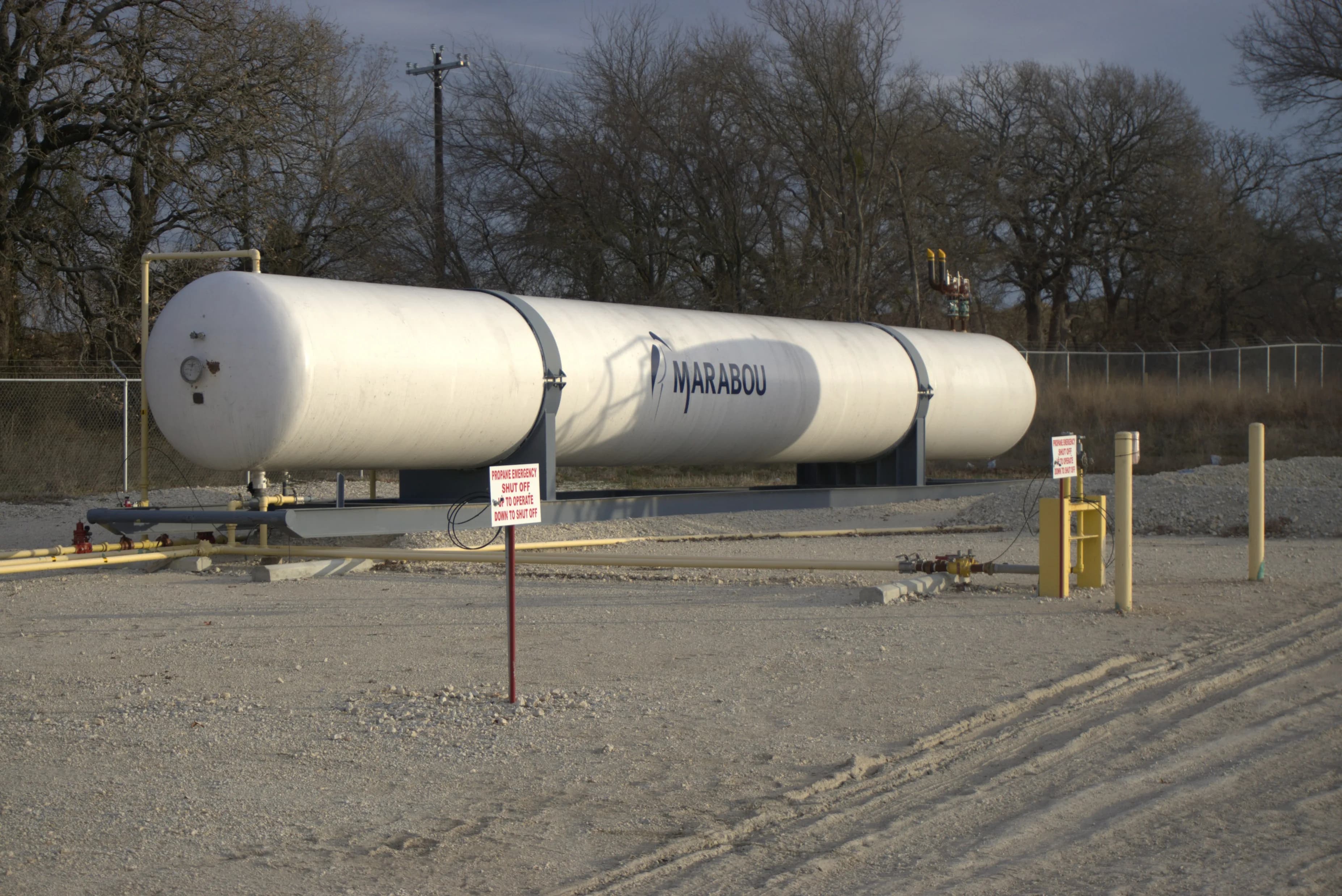 A horizontal bullet storage vessel on steel saddles at a fenced site, with connecting pipework and bollards on a graded pad